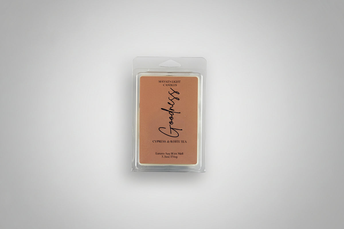 Plastic wax melt container with a brown label that reads Mayken Light Candles Goodness wax melt, scent of cypress and white tea on a white background