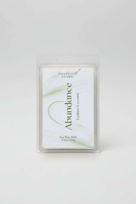 clear container with a white and green label for Abundance. Scents of Bamboo and coconut. 5.5 oz/156g