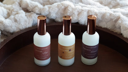 3 white bottles with gold lids. One has dark orange label named Autumn Refuge, one has a dark yellow label named Changing Seasons and one has a deep burgundy label named Faithful Harvest. 