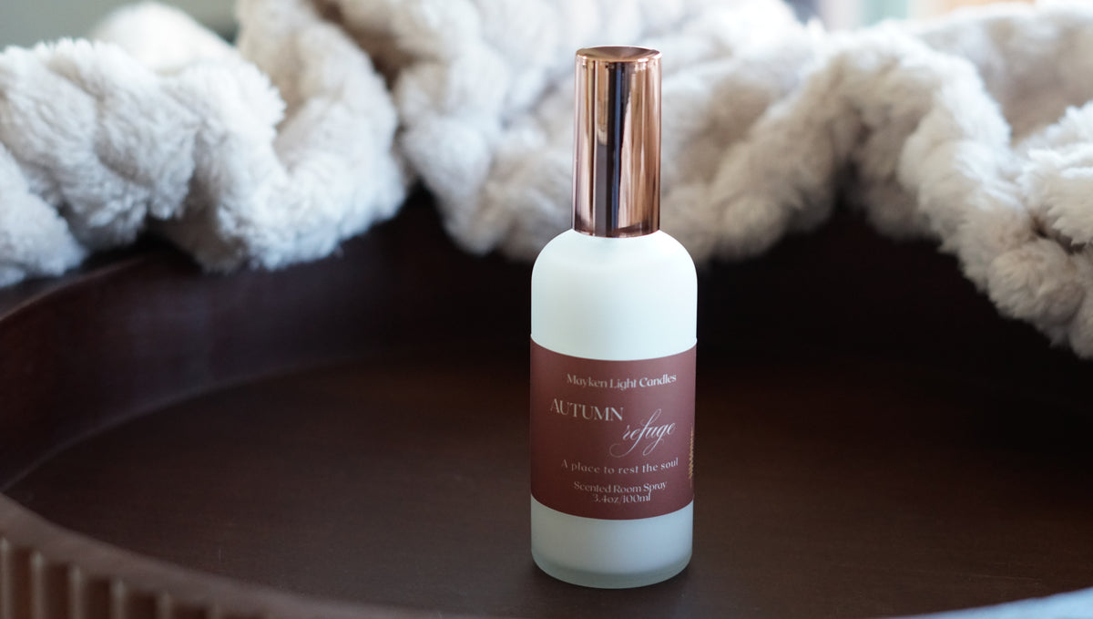 White bottle with dark orange label with the name Autumn Refuge Room Spray with a gold lid 