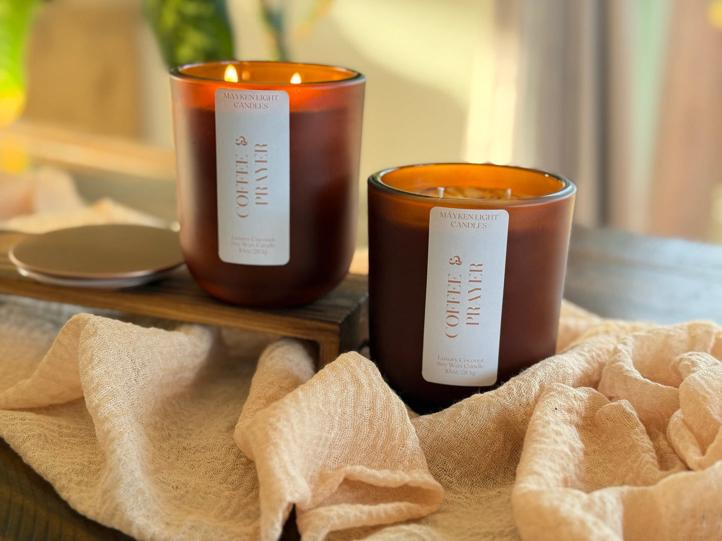 Two lit candles with labels on a wooden surface, surrounded by soft fabric.