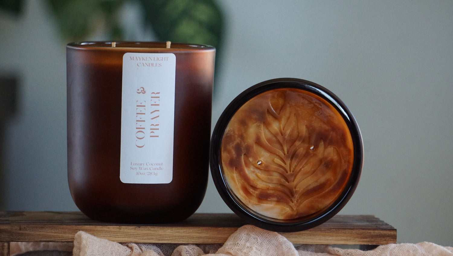 Brown candle with a label and a small dish with a coffee design on a wooden surface.