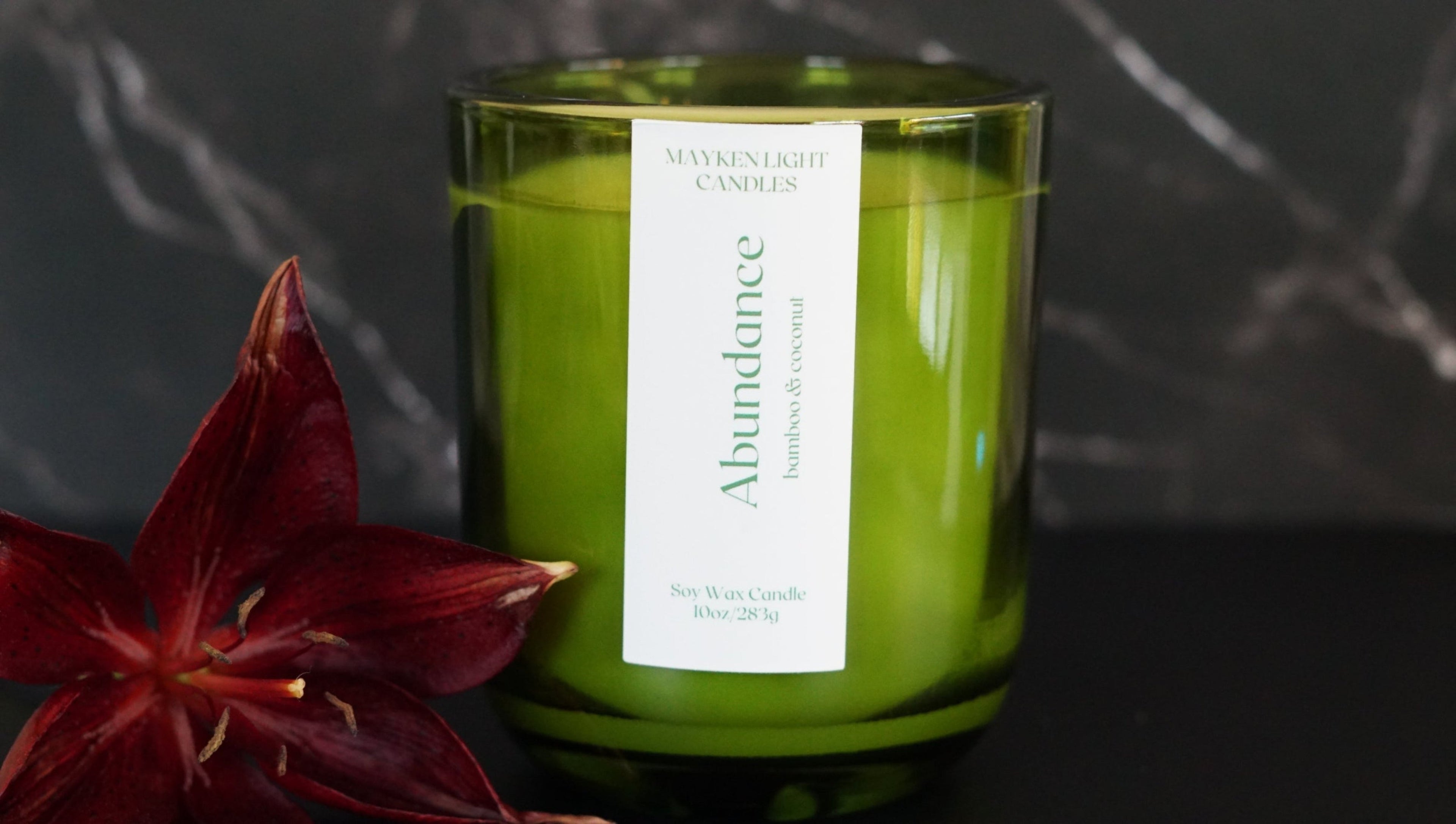 Green candle labeled 'Abundance' with a red flower on a dark background