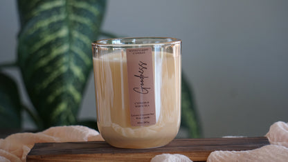 Candle with a label on a wooden surface, blurred green plant in the background