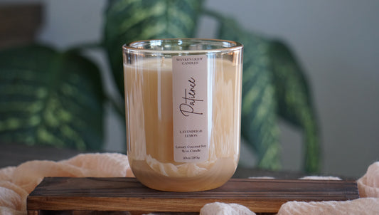 Candle with a label on a wooden surface, blurred green plants in the background