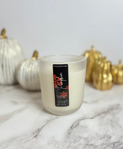 White Candle with a black label that reads Pumpkin in and has orange snowflakes in front of decorative pumpkins on a marble surface