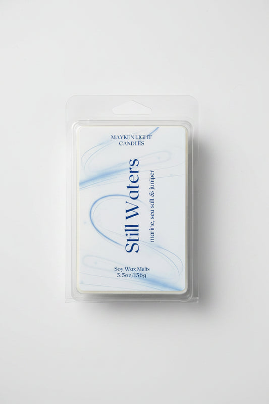 Clear container with white and blue label for Still Waters. Scent of Marine, Sea Salt, and Juniper. 5.5 oz/156g