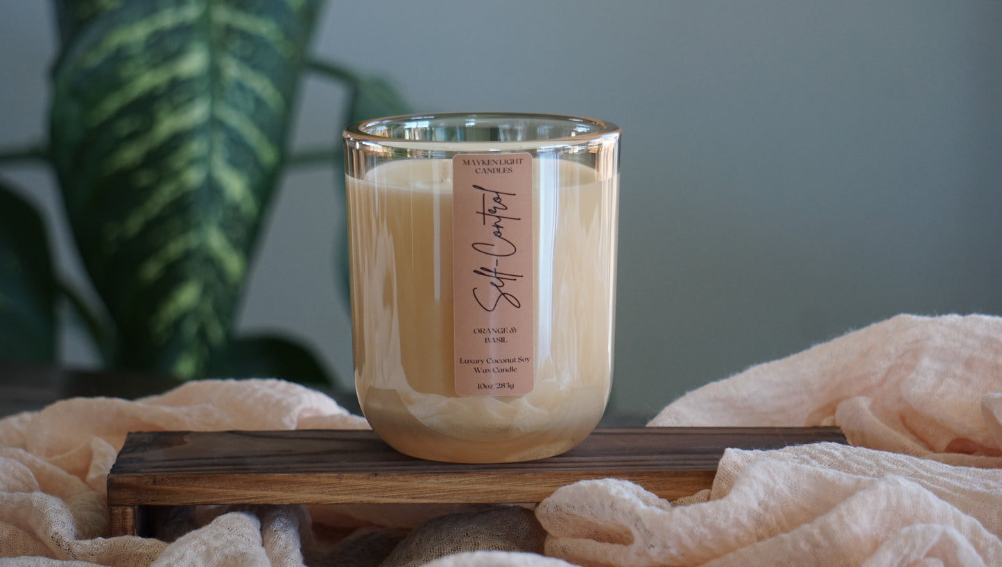 Candle with a label on a wooden stand, surrounded by soft fabric and a plant